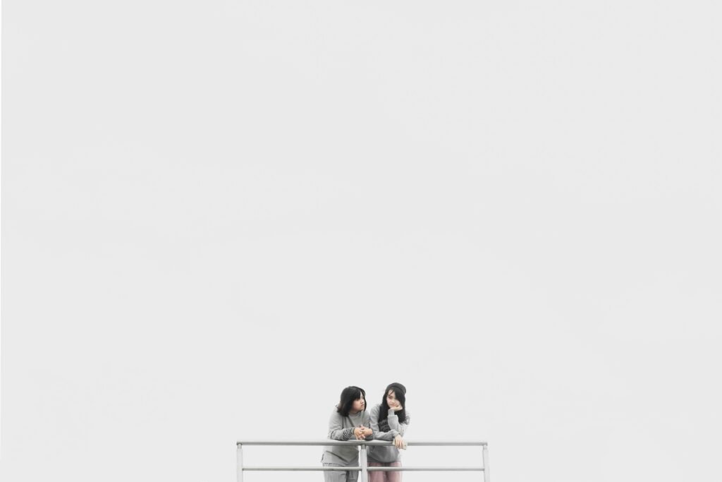 Two women on a balcony against a white background, expressing calmness. Jonas acadichon